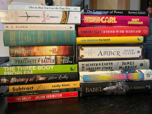 Pile of books: Tad Williams - The Dragonbone Chair, W.H. Auden - Selected Poems, Thomas Mann - Der Zauberberg, Terry Pratchet & Stephen Baxter - The Long Earth and The Long War, Cixin Liu - The Three-Body Problem, Kaliane Bradley - The Ministry of Time, List Klotz - Subtract, Dorothy Sayers - Whose Body? Julian Rubinstein - The Holly, Timothy Egan - A Fever in the Heartland, Cory Doctorow - The Bessel, Roger Zelazny - The Great Book of Amber, James McBride - The Heaven & Earth Grocery Store, Gabrielle Zevin - Tomorrow and Tomorrow and Tomorrow, R. F. Kuang - Babel, Matt Dinniman - Dungeon Crawler Carl, Rosemary Kirstein - The Lamguage of Power, Amal El-Mohtar & Max Gladstone - This Is How You Lose the Time War