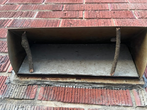 Exhaust vent in a red brick wall, the flap is forced closed by two sticks